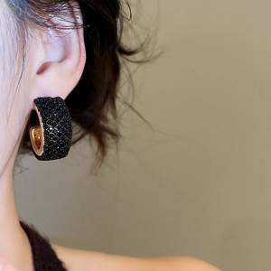 Close-up of a model wearing C-shaped gold earrings with sparkling black crystals