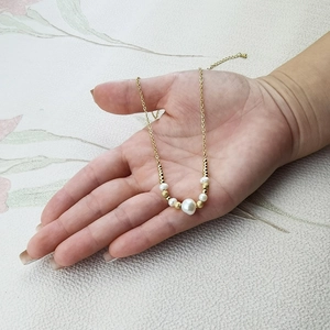 Detail view of a gold chain necklace with large and small pearls and frosted gold beads