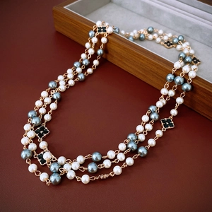 Detail of layered gold necklace with black clover charms and lustrous pearls