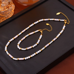 Elegant shell beaded jewelry set with gold cylinders on a black tray