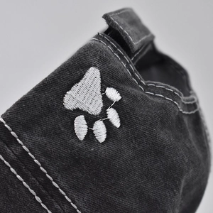 Detailed close-up of a white paw embroidery on a washed black cotton baseball cap side
