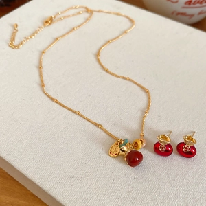 Detailed view of gold plated necklace and earrings set with red zircon money bag charms