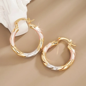 Detailed macro view of tri-color twisted hoop earrings with textured gold and silver finish