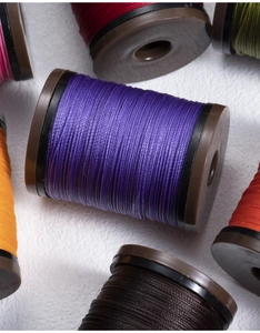 Macro shot of 0.4mm round waxed threads on bobbins in purple and various colors