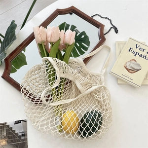 Détail d'un sac en filet tissé beige au design ajouré avec des fruits frais et des tulipes