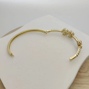 Golden open bangle featuring two floral designs inlaid with white cubic zirconia crystals
