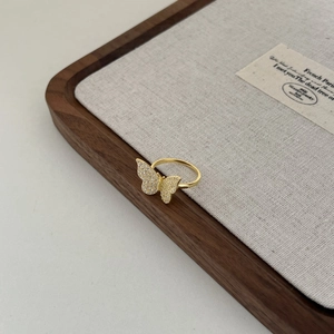 Detail of a gold butterfly ring with shimmering cubic zirconia on a wooden tray