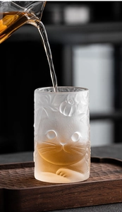 Detailed close-up of frosted glass cup featuring 3D embossed cat and persimmon patterns