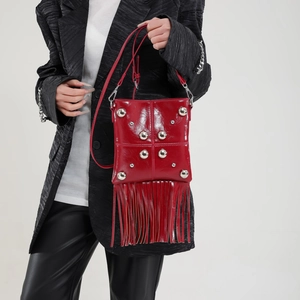 Red crossbody bag with silver studs and long tassels, shown on a professional model
