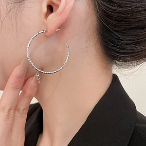 Close-up of a model wearing large silver textured hoop earrings with minimalist twist design