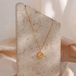 Macro detail of gold octagonal pendant with floral relief on a beaded chain necklace