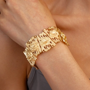Detailed view of wide golden matte metal bracelet featuring carved rose floral patterns