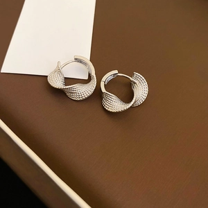 Macro detail of silver twisted hoop earrings with spiral texture on brown leather base