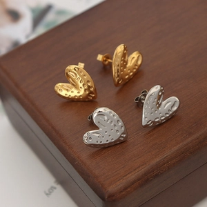 Golden and silver heart-shaped metal stud earrings with textured surface on wooden box