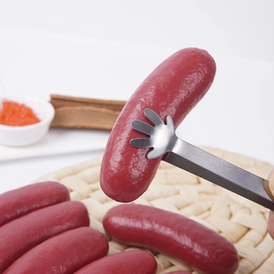 Mini stainless steel food tongs with hand-shaped grips picking up a realistic red sausage