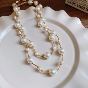 Detail of elegant gold beaded necklace with glossy white pearls on ceramic tray