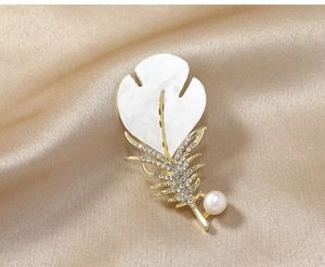 Elegant gold leaf brooch with crystals and pearl detail on silk background