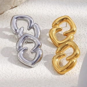 Close-up of polished gold and silver geometric interlocking loop earrings on stone