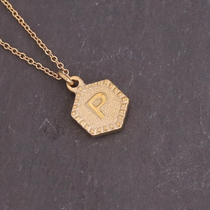 Detailed close-up of a golden hexagonal pendant with an embossed letter P and hammered texture