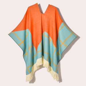 Orange and teal jacquard knitted poncho with yellow plaid pattern and beige fringe trim