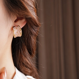 Gros plan d'une boucle d'oreille fleur rose émaillée avec finition dorée sur modèle