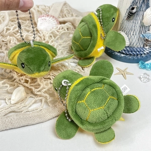 Three plush green sea turtle keychains with yellow bellies on a beach-themed background