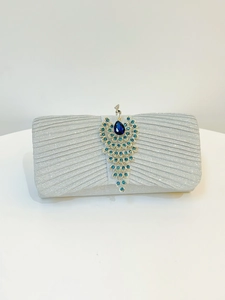 Macro detail of silver pleated evening clutch with crystal peacock brooch and blue gems