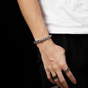 Men's silver braided chain bracelet and black decorative rings set on model wrist