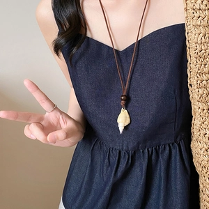 Detail of bohemian necklace featuring a natural cream shell pendant and dark cord strap