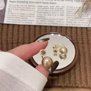 Detail view of golden pearl earrings with sun-shaped zircon studs held against a mirror