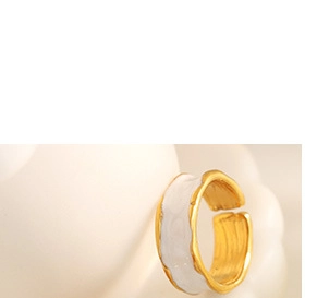 Detail of wave-pattern gold-plated ring with white enamel finish on a ceramic prop