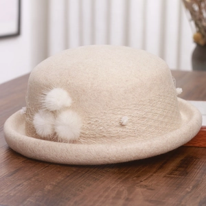 Close-up of beige wool felt cloche hat with mesh lace and plush pom-pom decorations
