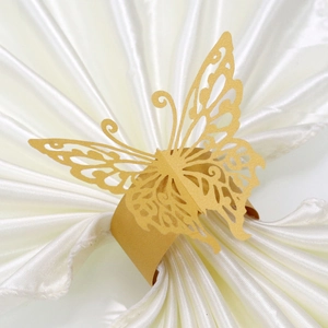 Close-up of a hollowed-out golden butterfly napkin ring on a white satin background