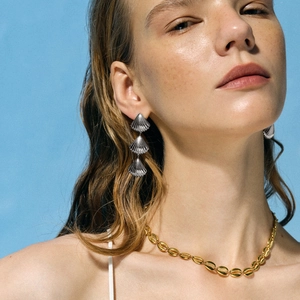 Close-up of ocean-themed seashell layered drop earrings and gold necklace on a model