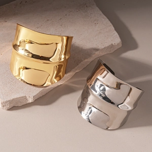 Irregular textured gold and silver metal cuff bracelets on natural stone background