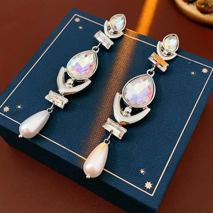 Close-up of silver long drop earrings with crystals and pearls on a blue jewelry box