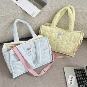Borse trapuntate in blu e giallo con tracolle rosa su un tappeto accanto al laptop