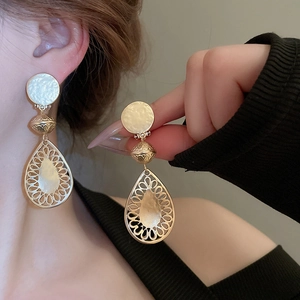 Close-up of gold hollow teardrop earrings with brushed metal texture on a model