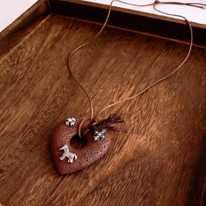 Macro shot of heart-shaped volcanic stone pendant with silver metal horse charm on wood