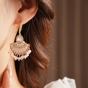 Détail de boucles d'oreilles dorées en éventail avec gemmes roses, perles et pompons perlés