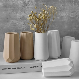 Assorted geometric ceramic flower vases in white and beige set on decorative books
