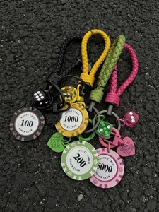 Macro detail of Monte Carlo poker chip and dice charms on a braided leather keychain strap