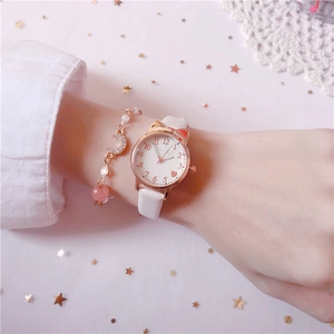 Detail of quartz watch with gold cat-ear case, white leather strap and crescent moon bracelet