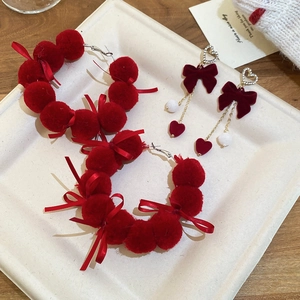 Detail of red velvet bow earrings with rhinestones and plush pom-poms on wooden desk