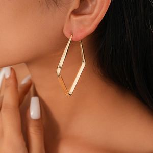 Close-up of a model wearing a geometric gold rhombus hoop earring with metallic finish