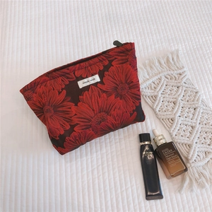 Detail of red and black floral jacquard makeup bag with woven label on white fabric