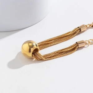 Detailed close-up of layered gold chain necklace featuring a bold metallic spherical pendant