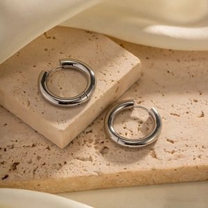 Macro shot of silver stainless steel hoop earrings on stone and silk background