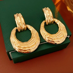 Close-up of gold chunky textured earrings on dark green display stand with warm lighting