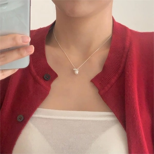 Detail of silver bow pearl necklace worn on red knit cardigan for elegant style